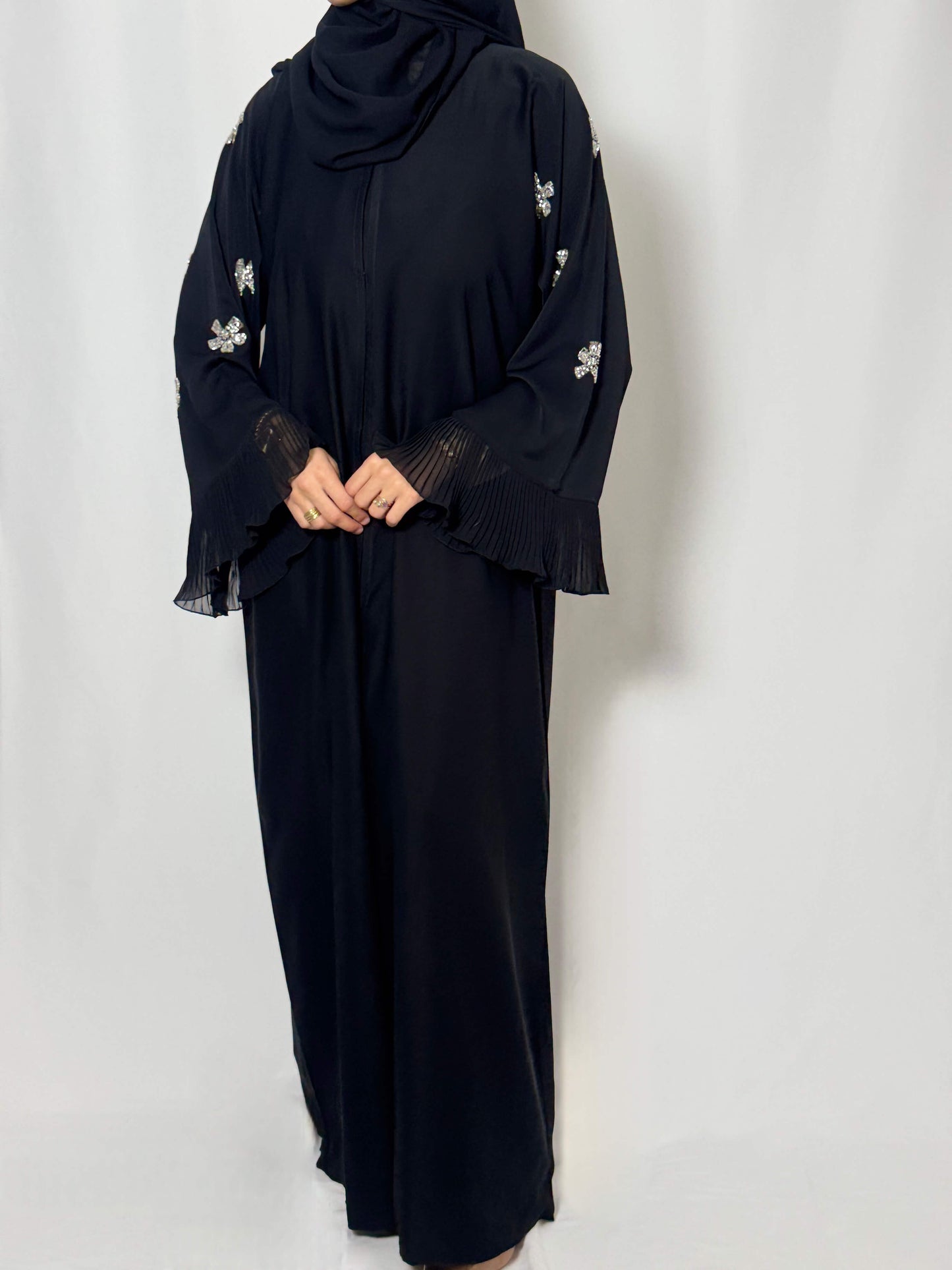 Abaya noire nejma fluide longue. les manches moderne sont ornée de de fleur et d'étoile en perles argenté. au bout des manche on retrouve un tissu légèrement volant plissée en transparence
