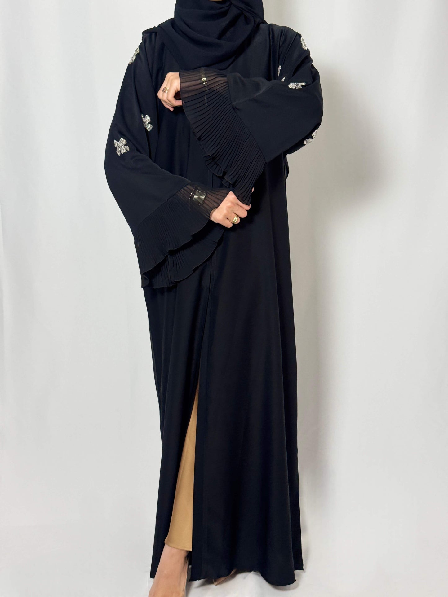 vue sur le smanches travaillé de la abaya noir nejma. mise en avant des voilage sur les manches. fond blanc photo studio