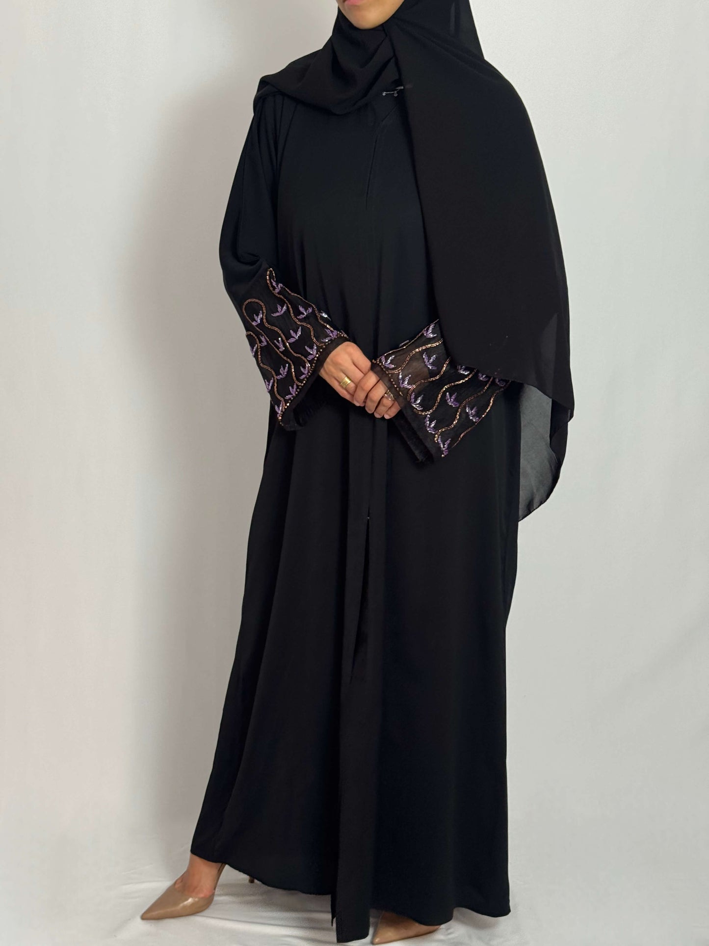 Abaya leila fluide et élégante raffinée tissus nidha. vue de face portée par une femme voilée sur fond blanc. abaya brodée aux manches avec des perles scintillantes aux couleurs lillas