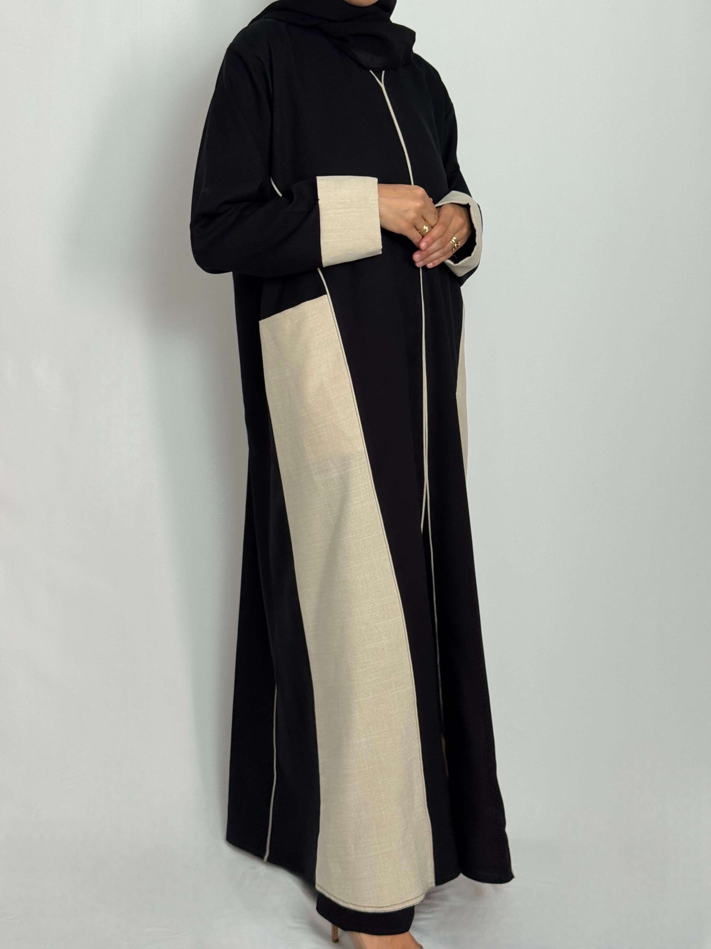 Abaya lina noir et beige vue de profil longue et fluide portée par une femme
