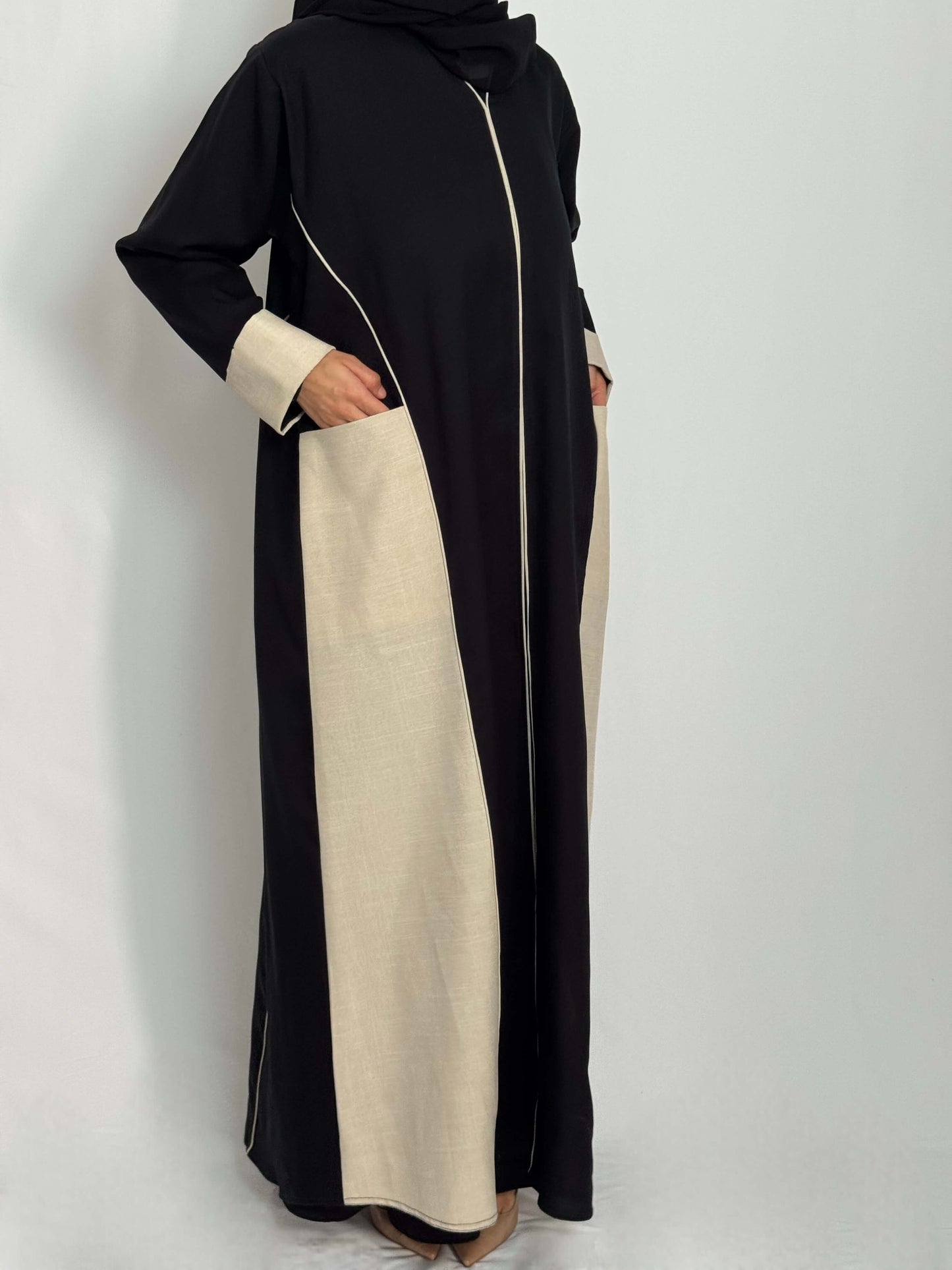 Silhouette de femme portant la abaya Lina noir avec des liserai beige et des poches