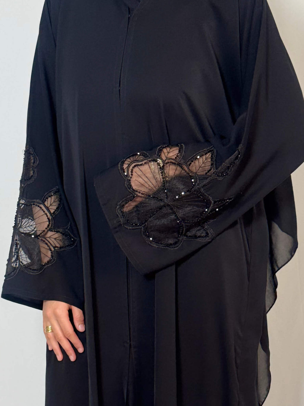 Zoom sur abaya noire avec dentelle fleuri en transparence sur les manches et perlage fait à la main