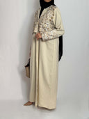 Abaya syria portée par une femme voilée tenue fluide beige vue de profil avec broderies sur le buste et les manches