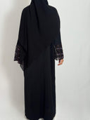 Abaya leila fluide et élégante tissus nidha vue de dos portée par une femme voilée sur fond blanc. abaya brodée aux  manches.